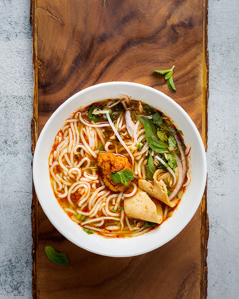 Noodles, tofu, and fried chicken piece in red-yellow broth with green garnish